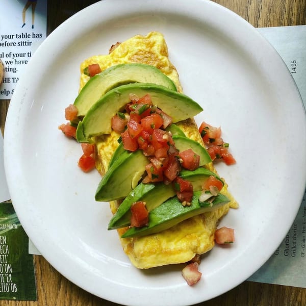 A fluffy omelet topped with sliced avocado and fresh pico de gallo on a white plate.