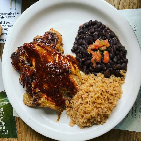 A plate of grilled chicken with a rich sauce, black beans topped with pico de gallo, and rice.