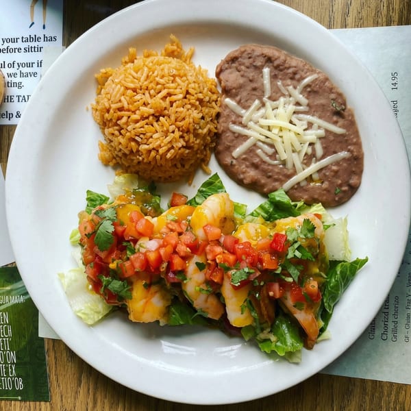 A white plate with shrimp and mango salsa on lettuce, rice, and refried beans with cheese.