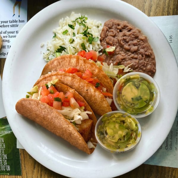 Three crispy tacos with lettuce and tomato, served with rice, refried beans, and guacamole.