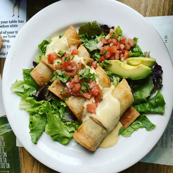 Crispy taquitos topped with queso, pico de gallo, and cilantro, served with fresh greens and avocado.