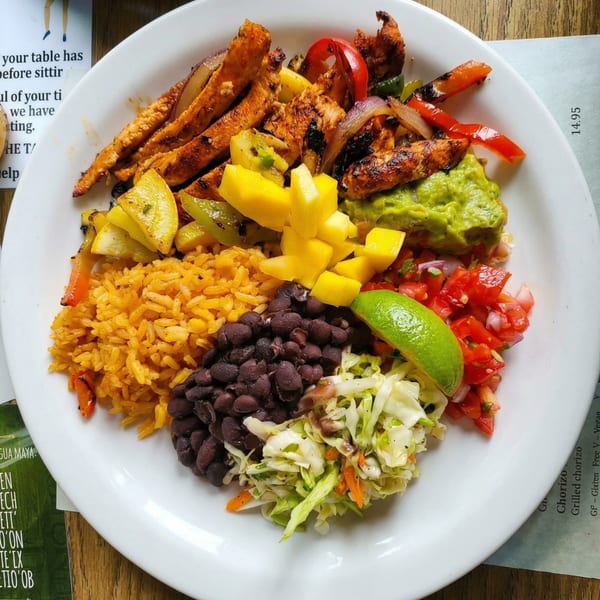 Grilled chicken fajita plate with rice, black beans, guacamole, salsa, mango, and coleslaw.