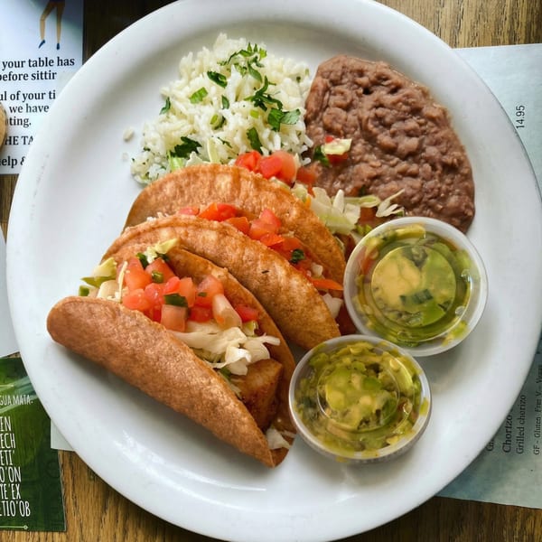 Three crispy tacos with lettuce and tomato, served with rice, refried beans, and guacamole.