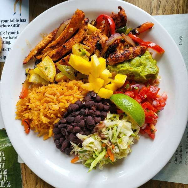 A vibrant plate of chicken fajitas with rice, black beans, guacamole, salsa, and mango.